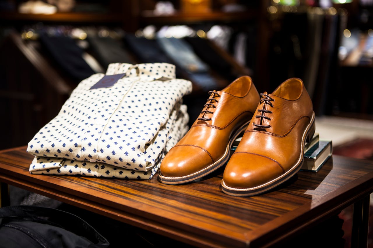 Home Elegant brown leather shoes and printed shirt displayed on a wooden table in a stylish clothing store.